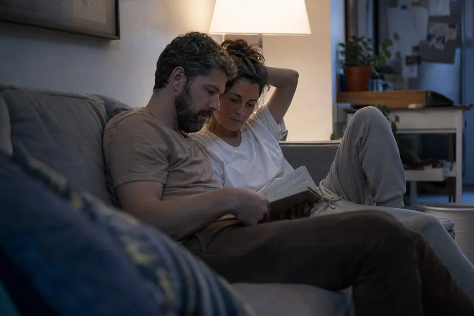 Couple reading a book together on a sofa in the evening under a lamp