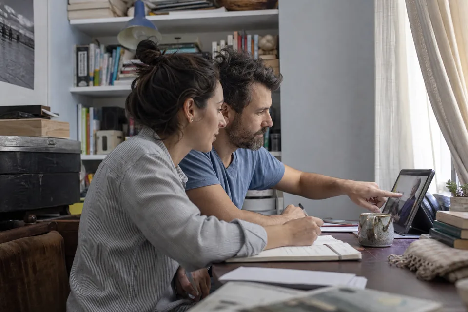 Husband and wife at a desk with a tablet and notebook working through a lesson together